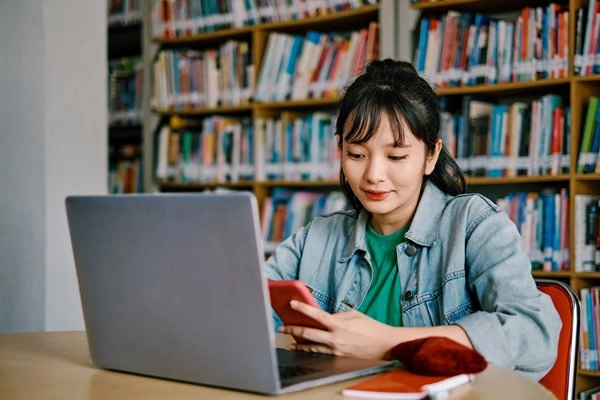 girl in a library on her phone and laptop