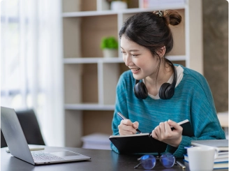 woman taking notes on a tablet while looking at a laptop